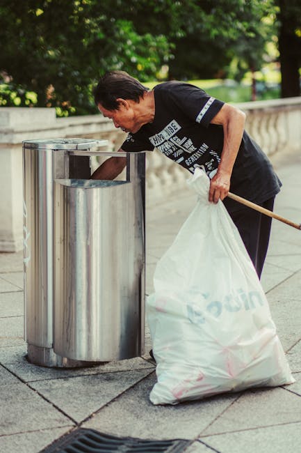 A black wheelie bin positioned on a sidewalk at night, labeled with the name 'St. John's' and a blank space for additional identification. The bin contains various types of waste including flattened c