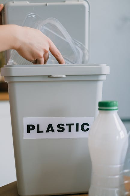 A person wearing an orange protective suit and white gloves is holding a large, tightly knotted blue plastic rubbish bag. The bag appears to be filled with waste and is held in the person's right hand